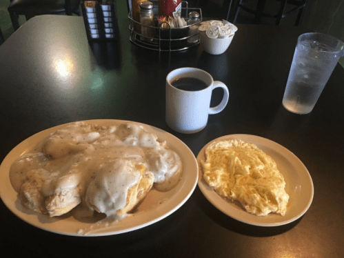 A plate of biscuits smothered in gravy, an omelet, a cup of coffee, and a glass of water on a black table.