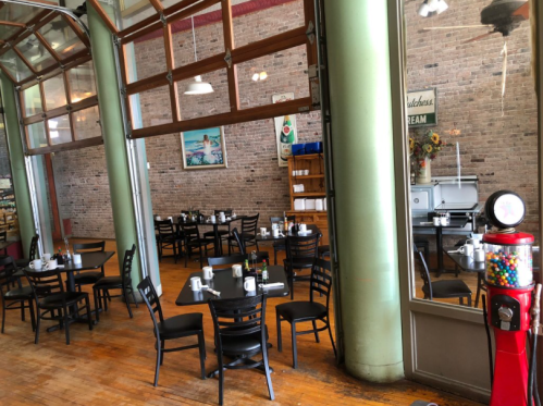 A cozy café interior with wooden floors, black tables, and a vintage gumball machine near large windows.