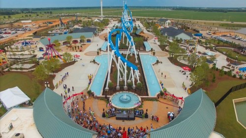 Aerial view of a water park featuring slides, pools, and a crowd gathered around a central fountain.