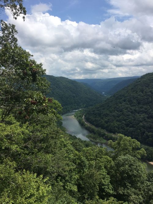 A scenic view of a river winding through lush green mountains under a partly cloudy sky.