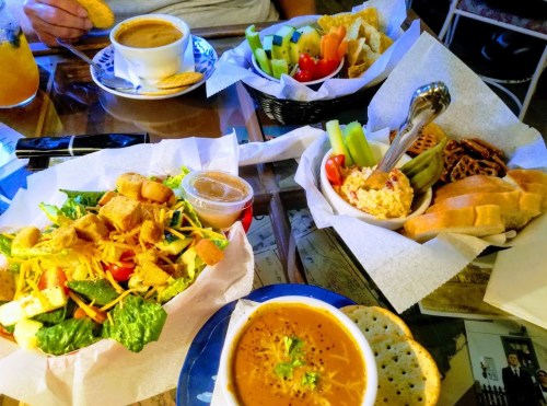 A table with a variety of dishes: salad, soup, fresh vegetables, and snacks, all served in baskets and bowls.