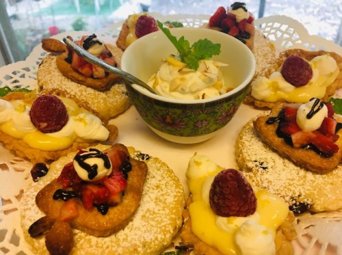 A decorative platter of pastries topped with fruit, cream, and sauces, accompanied by a bowl of whipped cream.