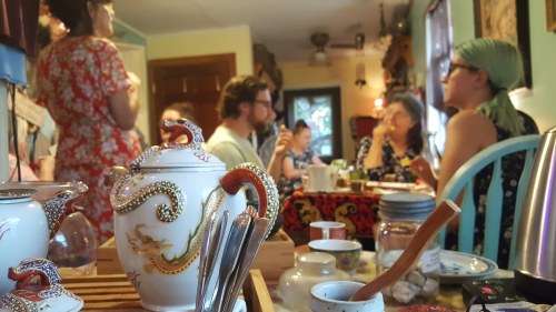 A cozy gathering with people enjoying tea, surrounded by colorful decor and a beautifully designed teapot in the foreground.