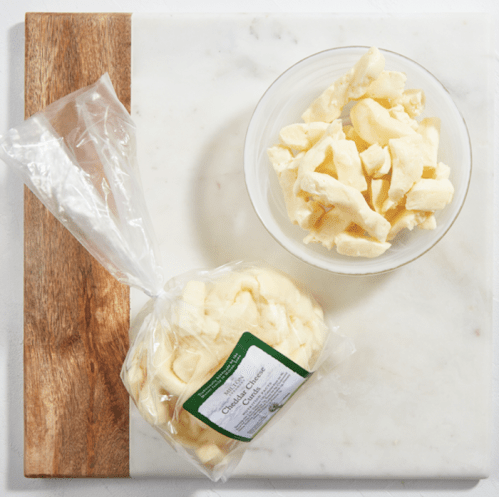 A bowl of cubed cheese next to a bag of cheese on a marble cutting board.