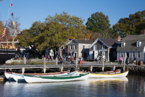 A scenic harbor with colorful boats, historic buildings, and people enjoying a sunny day by the water.