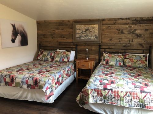 Cozy bedroom with two beds, wooden walls, and a horse painting. Colorful patchwork quilts add a warm touch.