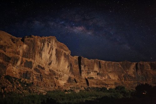 A starry night sky over a rugged canyon landscape, with cliffs illuminated by soft light.
