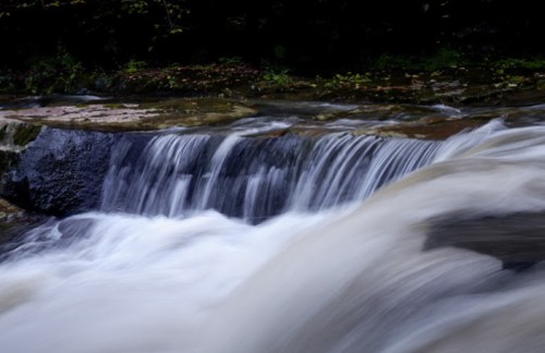 A serene waterfall cascades over rocks, creating a smooth flow of water in a tranquil natural setting.