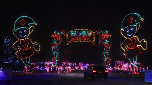 Colorful holiday lights form an archway with cheerful elves, welcoming visitors to a festive display at night.