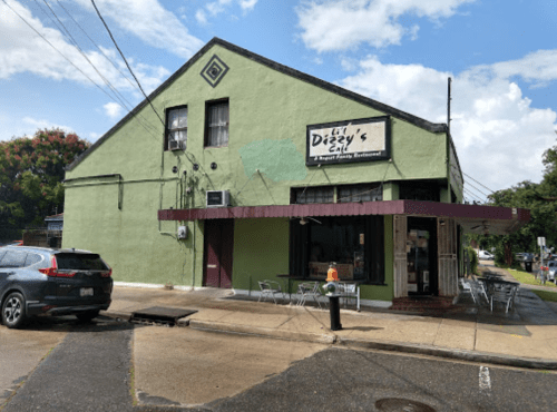 A green building with a sign for "Lil Dizzy's Cafe," featuring outdoor seating and a cloudy sky in the background.