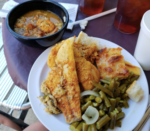 A plate of fried fish, chicken, green beans, and cornbread, with a bowl of shrimp stew and iced tea on the side.