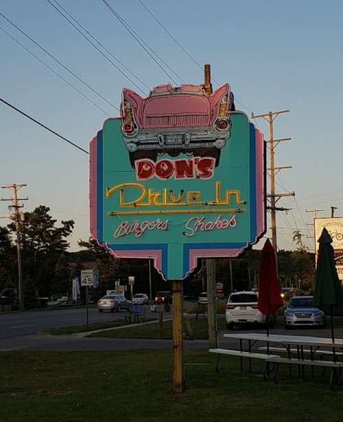 A colorful retro sign for Don's Drive-In featuring a classic car, advertising burgers and shakes.