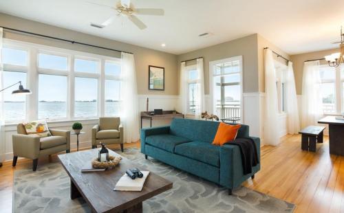 Bright living room with large windows, a teal sofa, wooden coffee table, and a view of the water. Cozy and inviting atmosphere.