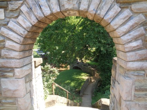 Stone archway framing a lush green landscape with a winding path and trees in the background.