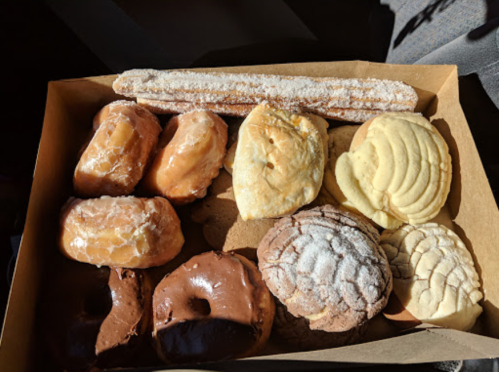 A box filled with assorted pastries, including donuts, conchas, and a churro, arranged neatly.