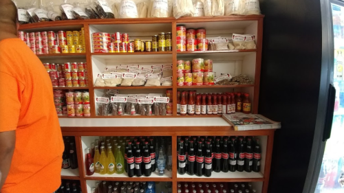 A shelf filled with various food products, sauces, and beverages, with a person in an orange shirt partially visible.
