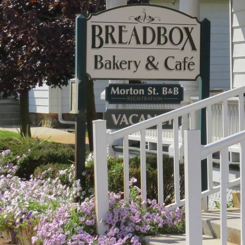 Sign for "Breadbox Bakery & Café" with flowers and a nearby building, indicating a B&B registration.
