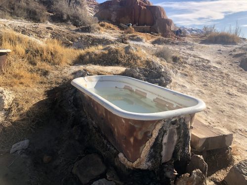 A rusty bathtub filled with water, set in a dry, rocky landscape with sparse vegetation.