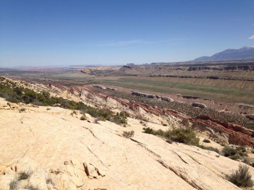 A panoramic view of a rocky landscape with layered cliffs and a vast valley under a clear blue sky.