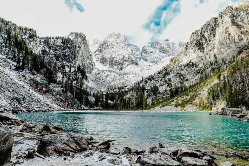 A serene mountain lake surrounded by snow-capped peaks and lush green trees under a partly cloudy sky.