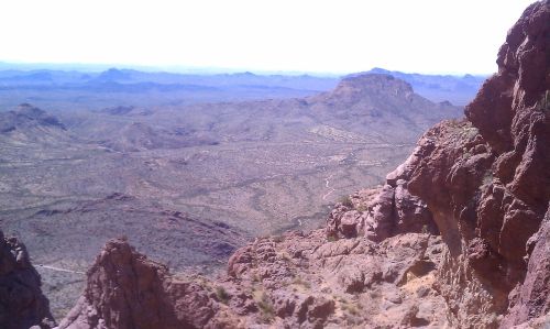 A panoramic view of rugged mountains and valleys under a bright sky, showcasing a vast desert landscape.