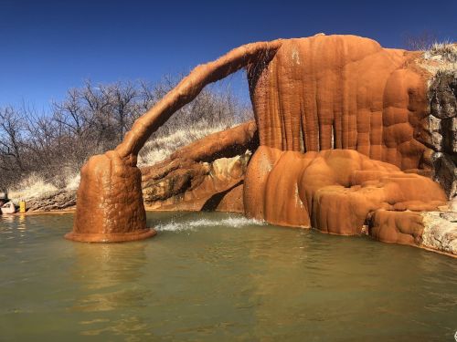 A natural hot spring with orange mineral deposits, creating unique formations beside a calm water pool.