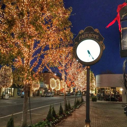 A street in Fairhope adorned with glowing holiday lights on trees, creating a festive evening atmosphere.