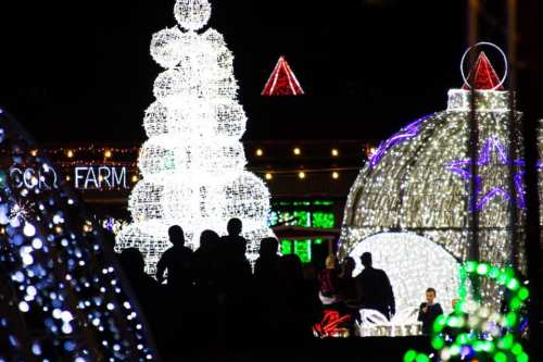 A festive display of colorful holiday lights, featuring a large illuminated tree and a dome, with silhouettes of people nearby.