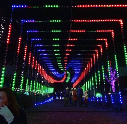 A colorful light tunnel with red, green, and blue lights, with people walking through it at night.