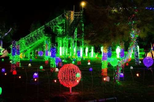 Colorful holiday lights illuminate a park at night, featuring glowing orbs and a decorated slide in the background.