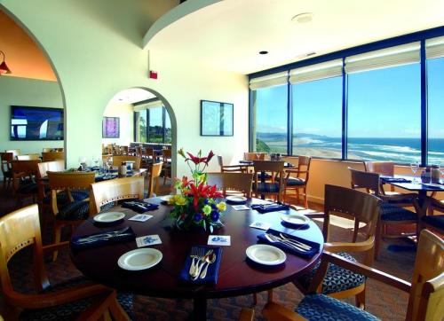 A dining area with a round table set for a meal, featuring large windows overlooking a scenic ocean view.