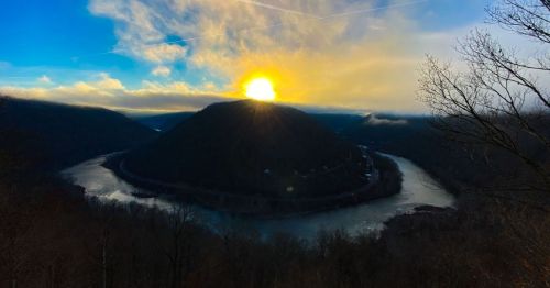 A scenic view of a river winding around a mountain at sunset, with vibrant colors in the sky and trees in the foreground.
