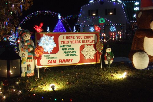 A festive sign reads, "I hope you enjoy this year's display. Merry Christmas, Sam Finney," surrounded by colorful holiday lights.