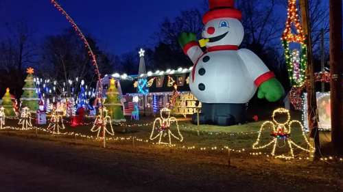 A festive display featuring a large inflatable snowman, decorated trees, and colorful lights in a nighttime setting.