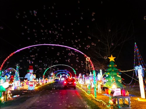 A festive night scene with colorful Christmas lights, decorations, and bubbles floating in the air along a decorated road.