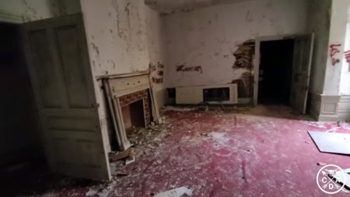Abandoned room with peeling walls, a fireplace, and scattered debris on a red carpet. Dark doorways lead to other areas.