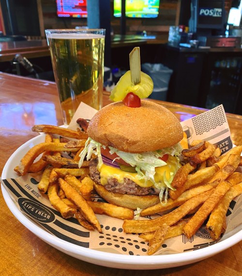 A juicy cheeseburger with lettuce, tomato, and pickles, served with crispy fries and a glass of beer.