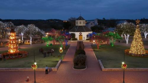 A festive park scene with colorful holiday lights, a decorated tree, and a charming building in the background.