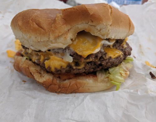 A half-eaten cheeseburger with melted cheese, lettuce, and a soft bun, resting on crumpled white paper.