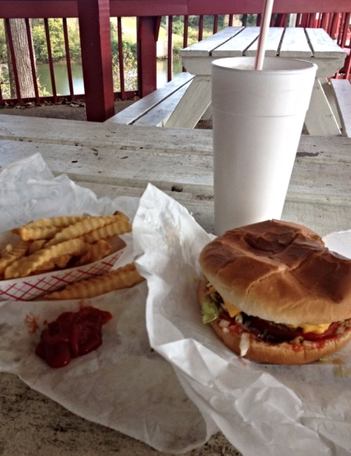 A burger with lettuce, tomato, and condiments, served with crinkle-cut fries and a large drink on a picnic table.