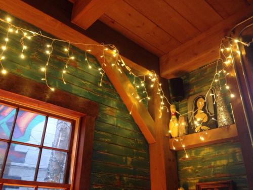 Cozy interior with green wooden walls, warm fairy lights, and a window showcasing a colorful mural outside.