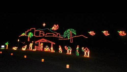 A colorful light display depicting a nativity scene with camels, palm trees, and stars against a dark background.