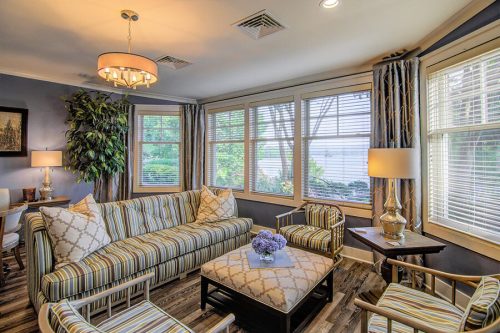 Cozy living room with striped furniture, large windows, and a coffee table adorned with flowers. Bright and inviting atmosphere.