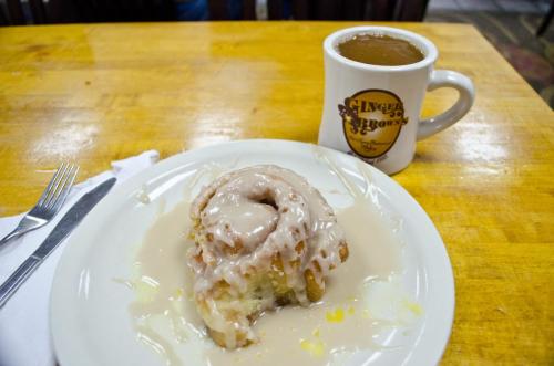 A plate with a glazed cinnamon roll and a cup of coffee on a wooden table.