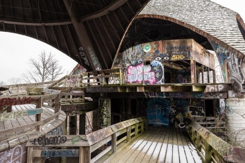 An abandoned structure with a wooden walkway, featuring colorful graffiti on walls and beams.