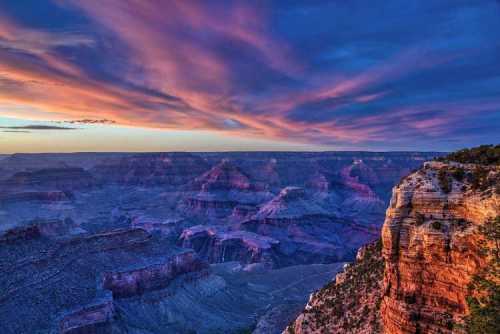 Vibrant sunset over the Grand Canyon, highlighting layered rock formations and colorful clouds in the sky.