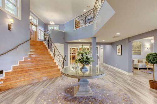 A spacious foyer with a wooden staircase, floral centerpiece on a round table, and modern decor in soft colors.