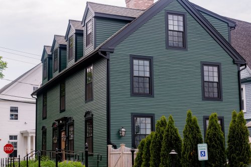 A green, multi-story house with black trim and large windows, surrounded by shrubs and a stop sign nearby.