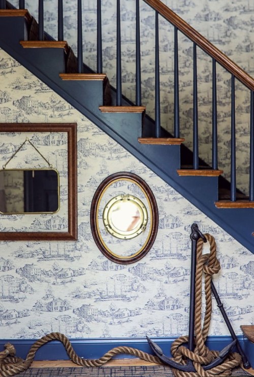 A staircase with blue railings, nautical-themed wallpaper, a round mirror, and an anchor with rope decor.