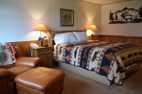 Cozy bedroom with a wooden bed, warm lighting, and a patterned blanket featuring wildlife motifs.